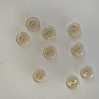 Dez botões brancos redondos com dois orifícios sobre superfície branca.