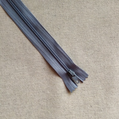 Fecho éclair cinza escuro sobre tecido bege com texto 'Cor 716'.