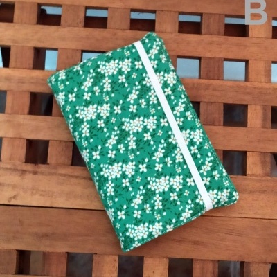 Carteira de tecido verde com flores brancas e elástico branco sobre superfície de madeira