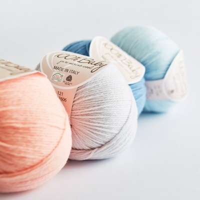 Quatro novelos de fio de algodão em tons pastel com etiquetas sobre fundo branco