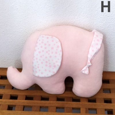 Almofada elefante cor-de-rosa claro com tecido branco e estrelas cor-de-rosa sobre madeira.