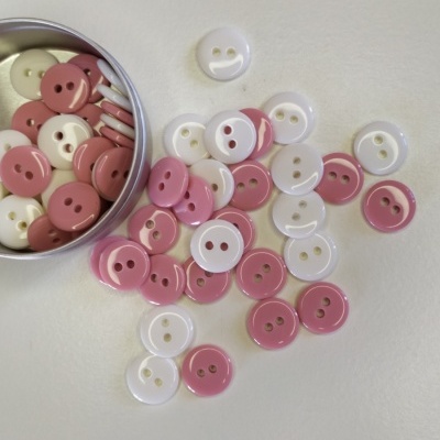 botões redondos brancos e rosa com dois furos em recipiente metálico sobre fundo branco