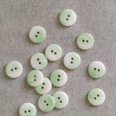 Botões redondos bicolor verde e branco sobre tecido cinza claro