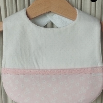 Babete de bebé branco e rosa com renda pendurado em cabide de madeira