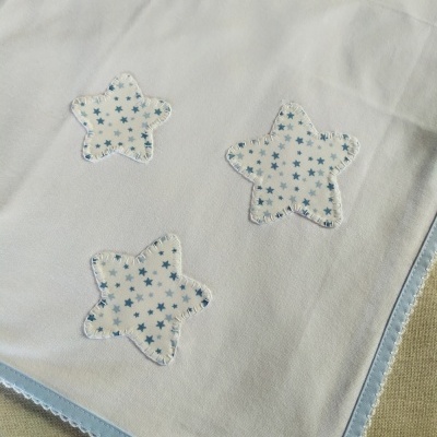 Cobertor branco com bordas azuis e estrelas aplicadas em tecido branco com padrão azul