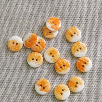 Botões redondos de madeira com pintura laranja sobre tecido cinzento