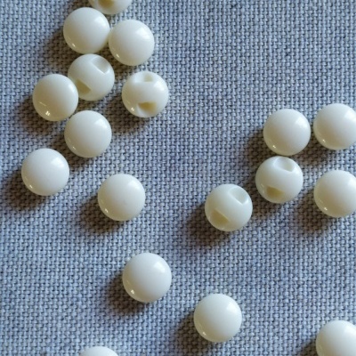 Contas brancas redondas de plástico com furo central sobre tecido cinzento.