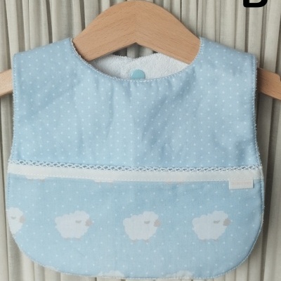 Babete azul claro com ovelhas brancas pendurado num cabide de madeira