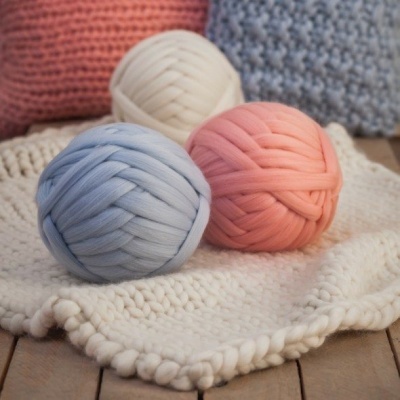 Bolas de fio grosso azul claro, creme e cor de rosa sobre manta branca de tricô