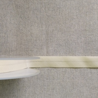 Fita têxtil bege claro com indicação 'Cor 14' sobre fundo de tecido cinzento
