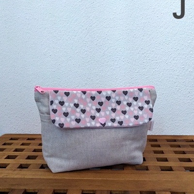 Bolsa cinza com aba rosa e padrão de corações, zíper rosa numa superfície de madeira