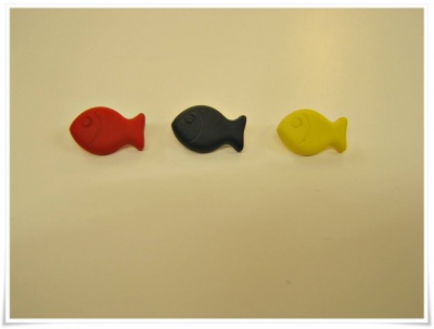 Ímanes em forma de peixe coloridos (vermelho, preto, amarelo) sobre superfície branca