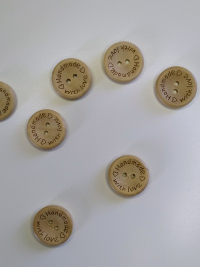Botões de madeira claros com inscrição 'Handmade with love' em superfície branca