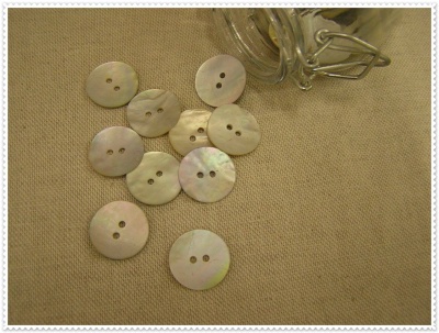 Botões redondos de madre-pérola sobre tecido bege com corrente metálica