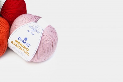 Novelo de lã rosa claro com rótulo DMC Merino Essentiel e outros novelos ao fundo