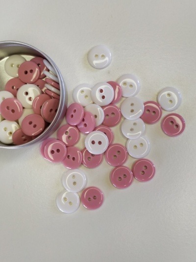 botões redondos brancos e rosa com dois furos em recipiente metálico sobre fundo branco