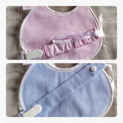 Dois babetes para bebé rosa e azul com padrões diferentes sobre tecido bege