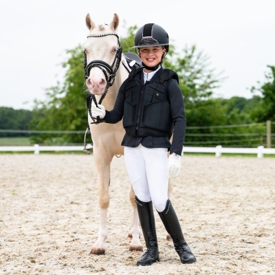 Criança com roupa de equitação e cavalo branco em pista de areia