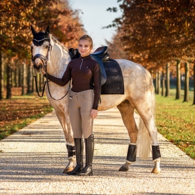 Menina com roupa de equitação a segurar cavalo numa alameda de outono