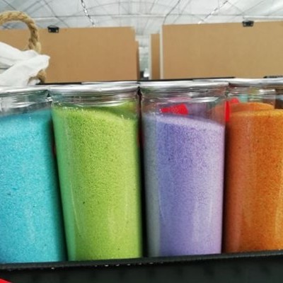 Quatro copos com areia colorida azul, verde, lilás e laranja em caixa preta