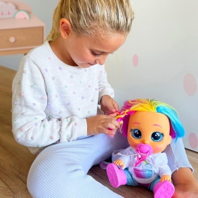 Criança com boneca de cabelo colorido e roupa branca sentada no chão em quarto infantil