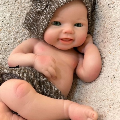 Boneco bebé realista com gorro e cueca castanhos reclinado em tecido bege