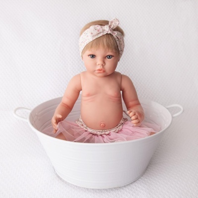 Boneca bebé realista com saia rosa e fita de cabelo sentada numa caixa branca