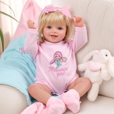 Boneca de bebé realista com roupa rosa e peluche de coelho branco num sofá claro