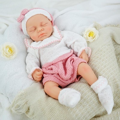 Boneca bebé realista deitada com roupa de malha branca e rosa