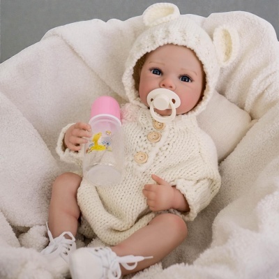 Boneca bebê realista com roupa branca e biberão rosa em almofada macia creme