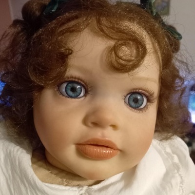 Boneca de porcelana com olhos azuis, cabelo castanho encaracolado e roupa branca