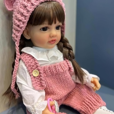 Boneca vestida com jardineira e gorro cor de rosa segurando chupeta rosa