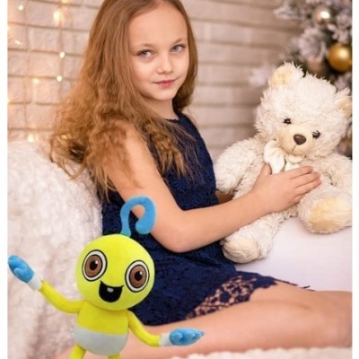 Menina com vestido azul segurando urso de pelúcia branco com brinquedo amarelo e azul em primeiro plano