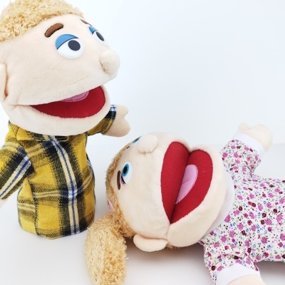 Dois fantoches de mão, um com camisa xadrez amarela e outro com roupa floral, sobre fundo branco.