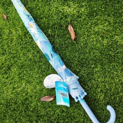 Guarda-chuva azul claro com padrão Stitch da Disney fechado sobre relva verde.