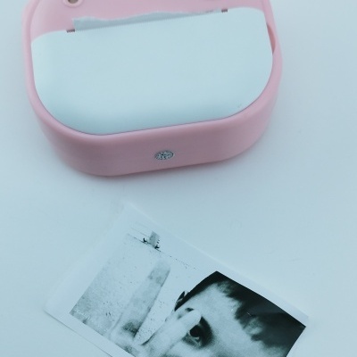 Impressora fotográfica instantânea rosa com foto a preto e branco de criança.