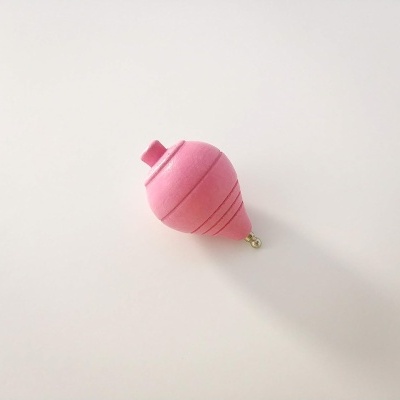 Pião rosa de madeira com linhas pretas numa superfície branca