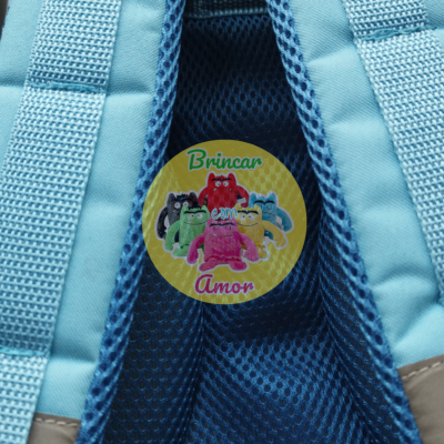 Mochila azul com alças acolchoadas e etiqueta colorida redonda com texto em português