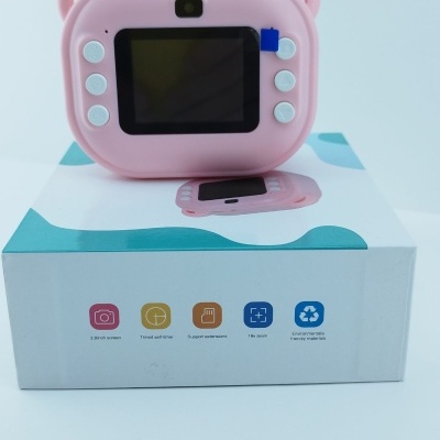 Câmara digital cor-de-rosa com ecrã e botões, sobre caixa branca com detalhes azuis e ícones coloridos