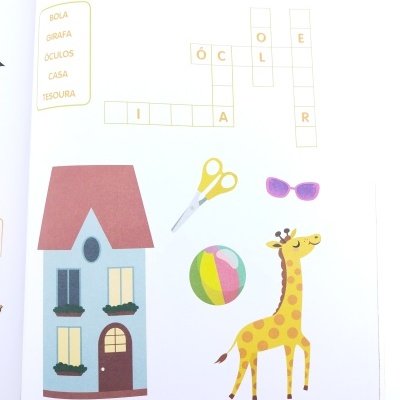 Livro infantil com palavras cruzadas e desenhos de casa, tesoura, óculos, bola e girafa.