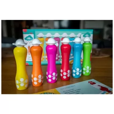 Sete garrafas plásticas coloridas com tampas brancas em formato de chapéu em cima de mesa de madeira.