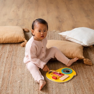 Criança vestida de rosa a brincar com xilofone amarelo num tapete com almofadas
