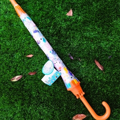 Guarda-chuva infantil laranja com padrão colorido sobre relva verde
