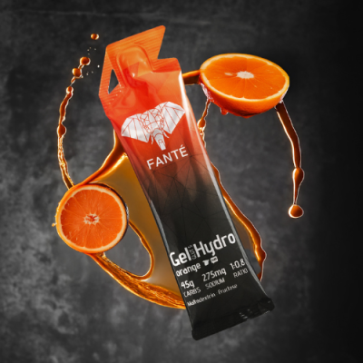 Embalagem individual laranja e preta de gel energético FANTÉ com fatias de laranja e gotas de suco em fundo escuro.