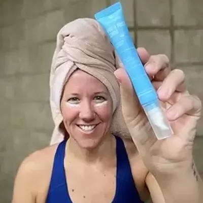 Mulher com toalha na cabeça segurando tubo azul claro de produto cosmético