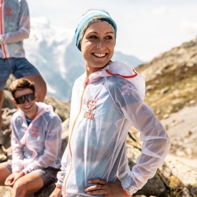 Mulher com jaqueta branca transparente com detalhes em laranja em área montanhosa rochosa