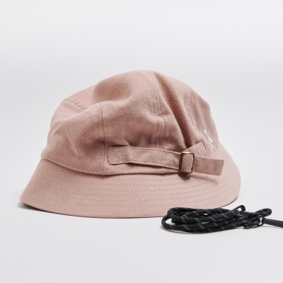 Chapéu rosa em tecido com cordão preto ao lado sobre superfície branca