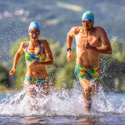 Homem e mulher a correr na água com fatos de banho e bonés coloridos