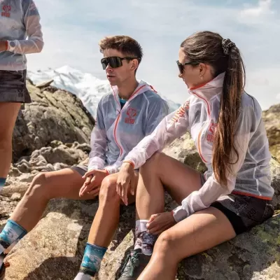 Homem e mulher em casacos leves cinza com texto vermelho sentados em rochas no monte