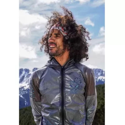 Homem com jaqueta cinza translúcida e faixa de cabeça em cenário montanhoso